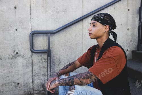 Preview: Young African American woman wearing black bandana and vest sits outside with a serious expression
