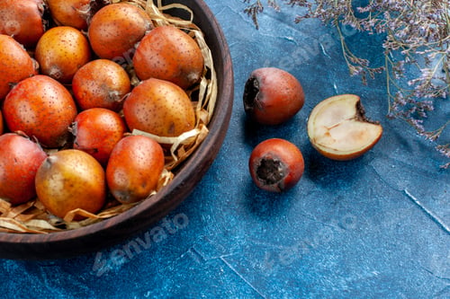 Preview: Half shot of whole and chopped mespilus germanica in a brown bowl on blue background