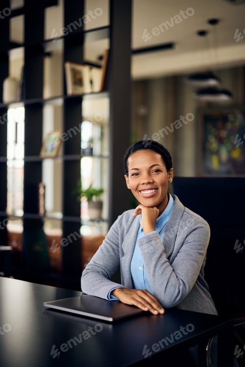 Preview: A smiling African woman posing for the camera while sitting at the office.