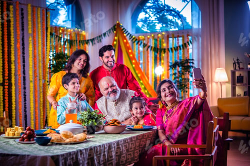 Preview: Portrait of happy Indian family in traditional outfit celebrating Diwali at home eating food