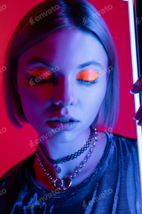 Preview: portrait of woman with neon makeup in blue light of glowing lamp on carmine red background