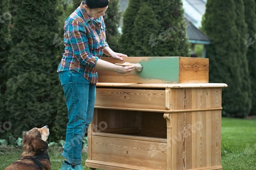 Preview: Woman painting a wooden furniture while sitting with her dog in the garden. DIY concept.