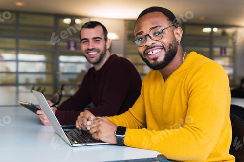 Preview: Positive diverse guys with laptop and tablet in modern workspace