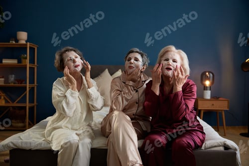 Preview: Senior women applying anti-aging cotton facial mask having fun together