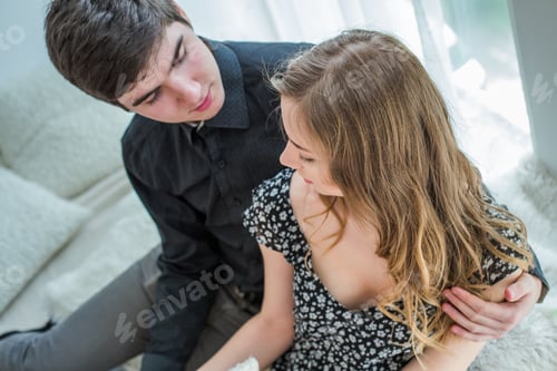 Preview: A guy in love hugs a beautiful long-haired girl sitting by the window.