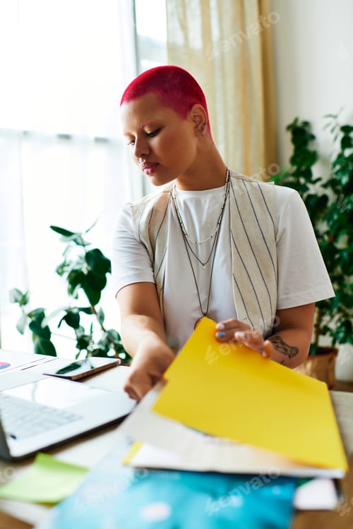 Preview: A young woman organizes documents at her home workspace during a sunny afternoon