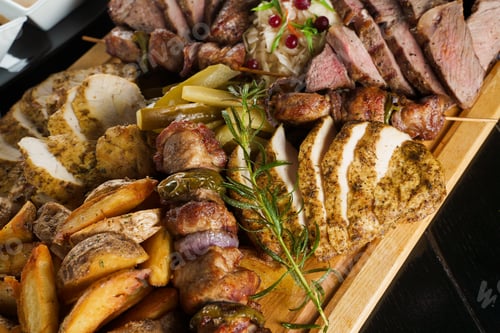 Preview: Barbecue pork kebab with roasted potatoes and assorted sausages served on black plate.