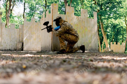 Preview: in the wild near tree structures player in a pintball uniform holds a pistol with a blue balloon