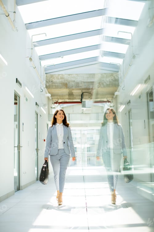 Preview: Pretty young business woman walking with briefcase in the office hallway