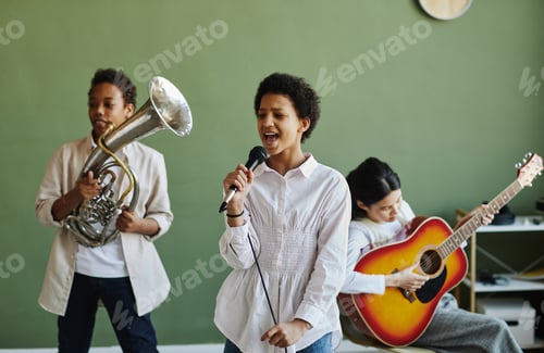 Preview: Happy youthful schoolgirl with microphone performing song with classmates