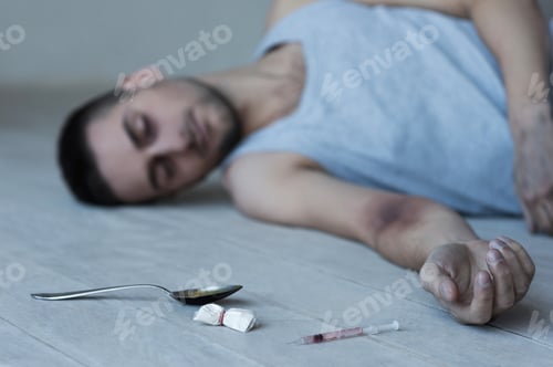 Preview: Heroin addict. Young man lying on the floor with syringe and pack of heroin laying near him
