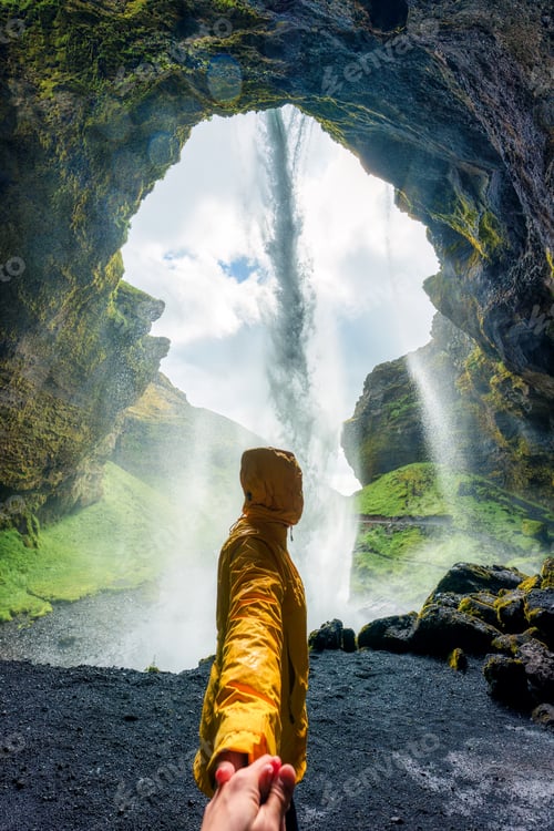 Preview: Back view of female tourist holding hand inside rocky canyon and Kvernufoss waterfall in summer