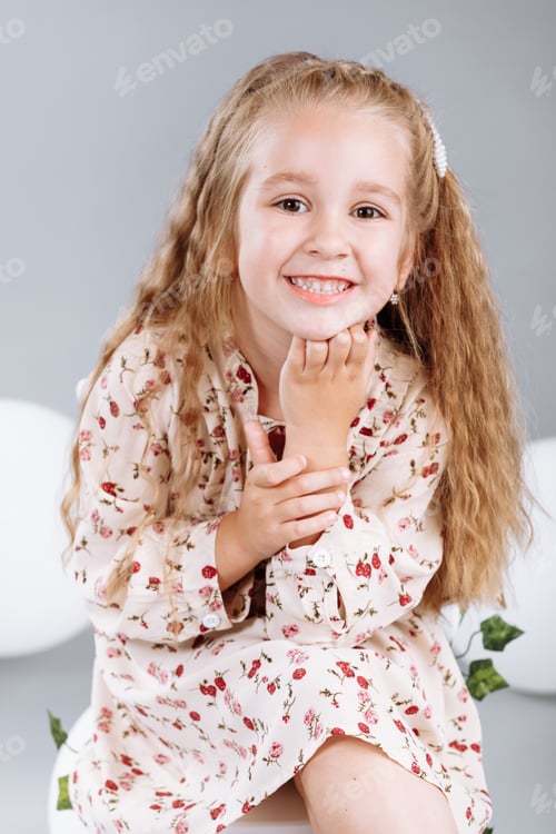 Preview: Cute little girl blonde smiling having fun in studio with white balloons and green. child in floral
