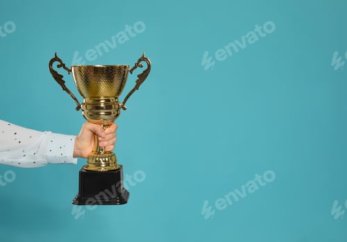 Preview: Young woman holding gold trophy cup on blue background, closeup with space for text