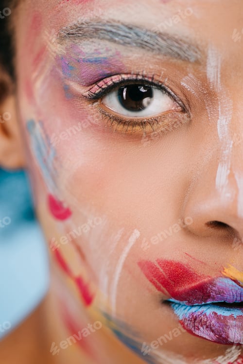 Preview: cropped shot of young woman with colorful strokes on face looking at camera on blue