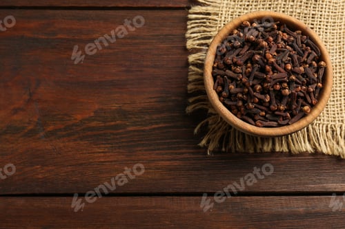Preview: Aromatic dry cloves in bowl on wooden table, top view. Space for text