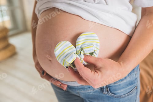 Preview: Belly of pregnant woman. baby shoes on pregnant belly. The concept of clothing becomes small due to