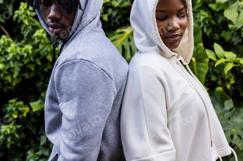 Preview: African american couple wearing white and grey hooded sweatshirts standing back to back in garden
