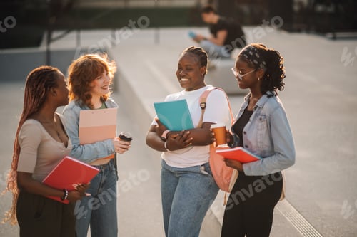 Preview: Happy diverse college girls on stairs at campus chatting and smiling.