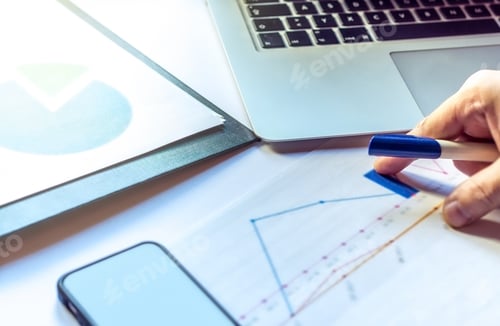 Preview: Office desk with hand pointing at charts and graphs with computer and smartphone