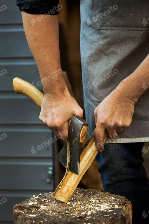 Preview: A craftsman holding a small axe, cutting down a small piece of wood on splitting block covered in