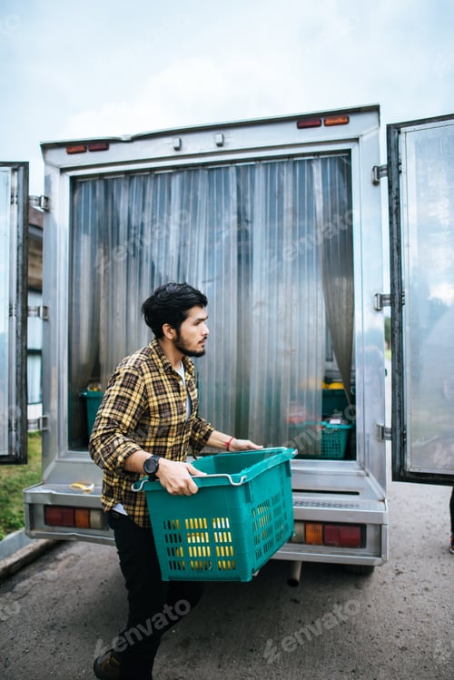 Preview: Portrait of a hipster farmer holding box of fruit lift up to the car to go market for sell.