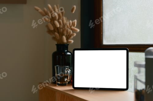 Preview: Digital tablet with empty screen beside a glass cup of tea on a wooden counter