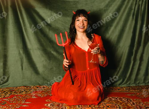 Preview: Portrait of a woman in a red dress with horns and a trident holding a red cocktail