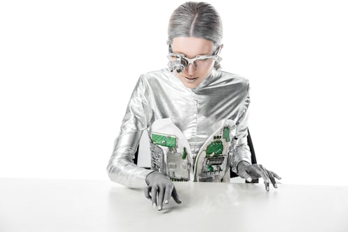 Preview: silver robot with eye prosthesis sitting at table and touching something on tabletop isolated on