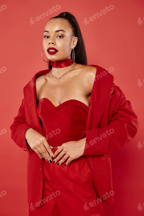 Preview: exquisite african american woman with ponytail posing in vibrant suit on red background