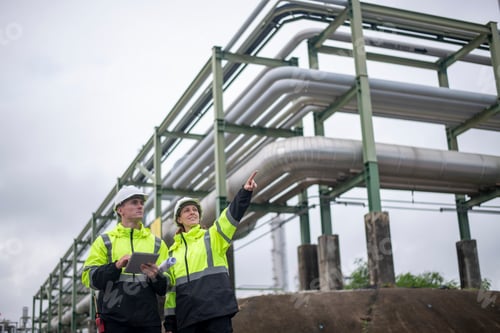 Preview: Engineers wearing safety gear, including hard hats examining survey a standing industrial facility g