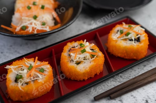 Preview: Sushi is in a plate with chopsticks and dipping sauce on a white cement floor.
