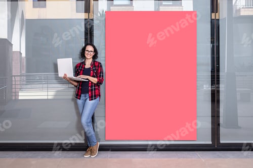 Preview: Saleswoman facing the camera with a laptop next to a shop window outdoors