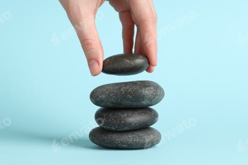 Preview: Woman making stack of stones on light blue background, closeup. Harmony and life balance