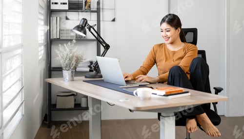 Preview: Beautiful young woman in casual clothing using laptop and smiling while working at home office.