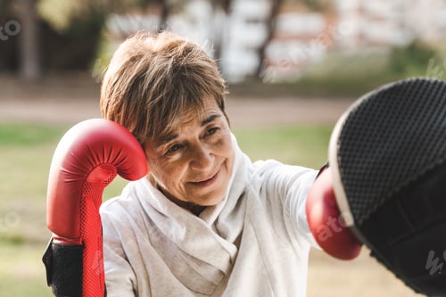 Preview: Senior woman doing boxing workout training with personal trainer outdoor at city park