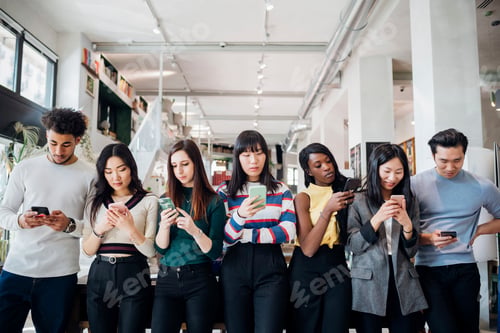Preview: Group of young businesswomen and men in a row, looking at smartphones