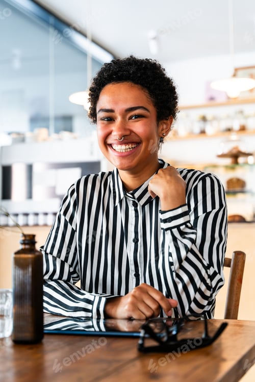 Preview: Beautiful young african woman with short hair sitting in a bar cafeteria