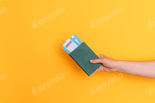 Preview: Hand holding a passport with tickets against a yellow background