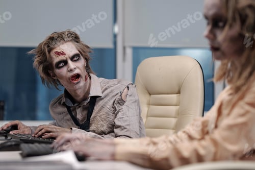 Preview: Zombie businessman with greasepaint on face and hands sitting by workplace and looking at co-worker