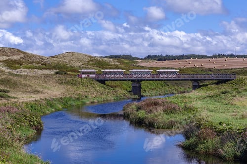Preview: Train crossing bridge over river with scenic hills.