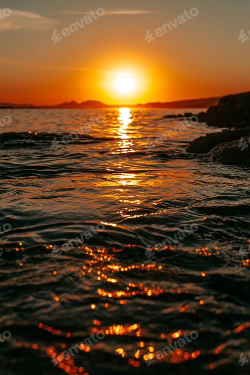 Preview: A close up of the sea through the rocks in the coast with a massive orange sunset