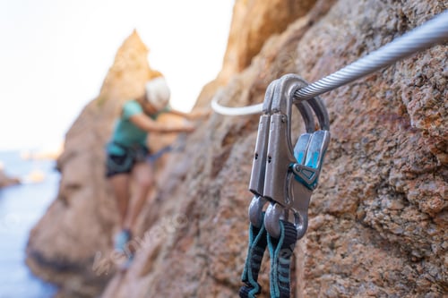 Preview: Pretty female climber strong success hiking on rocks over the sea with rope and helmet.