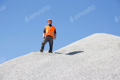 Preview: Construction worker surveying the site from atop a gravel mound