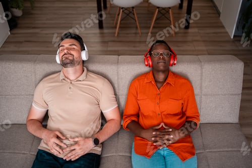 Preview: Two men relaxing on a sofa enjoying music through headphones in a cozy living room