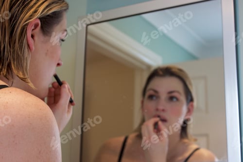 Preview: Brunette Woman looking in mirror Applying lipstick
