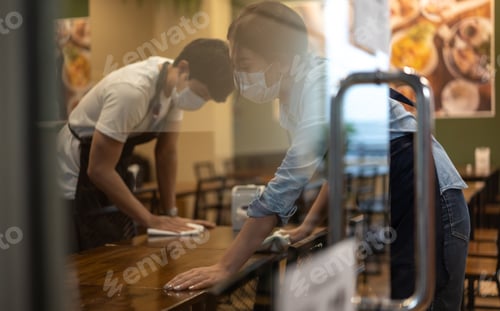 Preview: Waiter wearing protective face mask while cleaning tables in restaurant