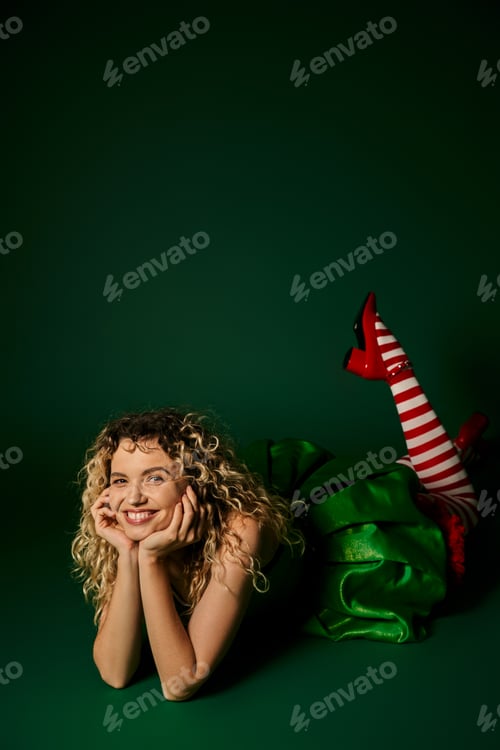 Preview: happy woman dressed as new year elf posing on floor with her legs slightly raised on green backdrop