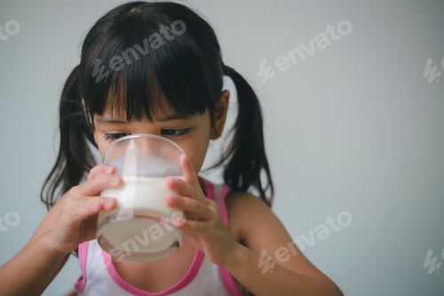 Visualização: Menina asiática está bebendo leite de um copo, ela estava muito feliz.