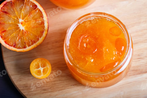 Preview: Orange and kumquat jam in a glass jar with fresh fruits on a wooden kitchen board.